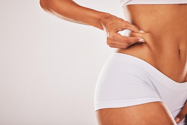 Foto peso gordo e mulher tocando seu estômago isolado em um fundo de estúdio cinza com espaço de maquete celulite de pele e mãos de uma modelo sentindo seu corpo por insegurança saúde e abdominoplastia