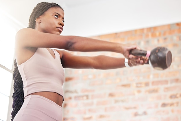 Peso de pesas rusas de fitness y mujer negra haciendo ejercicio con motivación de fuerza y salud en un gimnasio Enfoque deportivo y atleta africana haciendo ejercicio de entrenamiento muscular en un centro deportivo