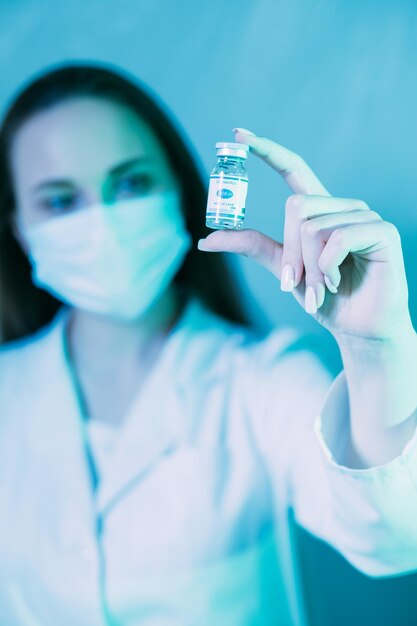 Pesquisa de vacinas Cura de coronavírus Segurança de imunização Cientista feminina em óculos de proteção facial de jaleco branco médico testando dose de frasco em fundo azul desfocado