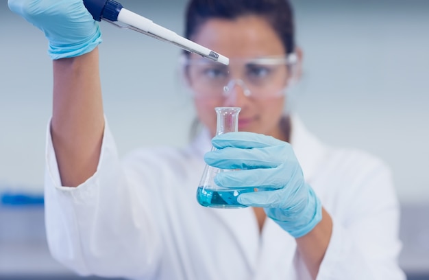 Pesquisador com líquido azul em balão e pipeta em laboratório