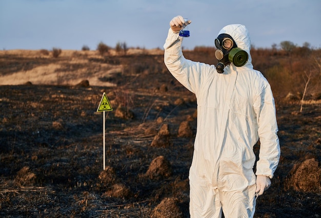 Pesquisador em traje de proteção trabalhando em um campo queimado coletando amostras de flora