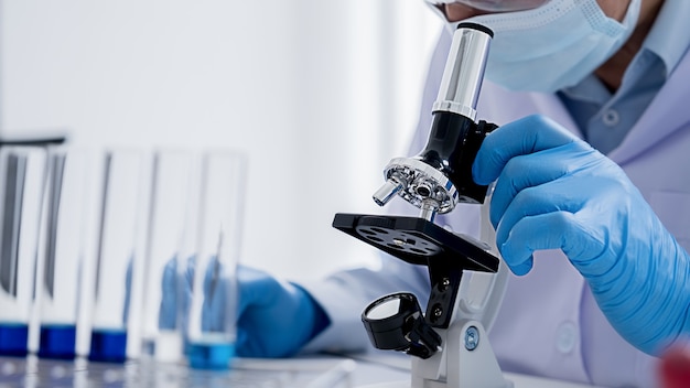 Pesquisador médico ou científico ou médico humano olhando para um tubo de ensaio de solução clara em um laboratório
