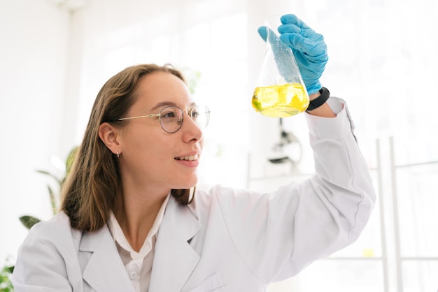 Pesquisadora cientista mulher caucasiana usando óculos agitando substância no frasco cônico para análise de líquidos no laboratório Cientista trabalhando com um conta-gotas e o frasco cônico