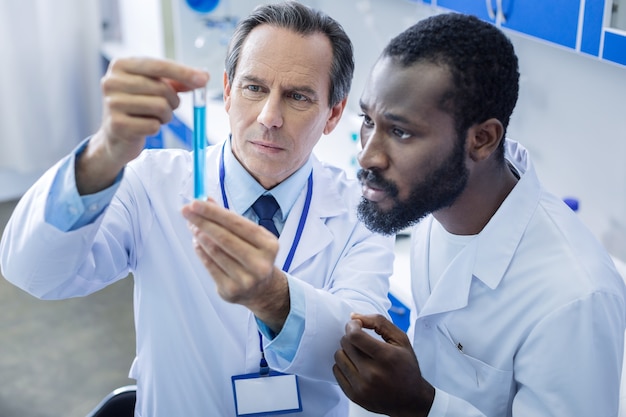 Pesquisadores profissionais. cientistas homens sérios e espertos, parados juntos e olhando para o tubo de ensaio, enquanto estão juntos no laboratório