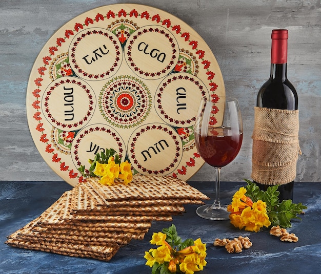 Pessach-Feier-Konzept Jüdischer Feiertag Pessach Hintergrund mit gelben Blumen mit Glas Wein Matza und Teller mit Seder auf blauem Hintergrund Traditionelle hebräische Inschriften auf dem Teller