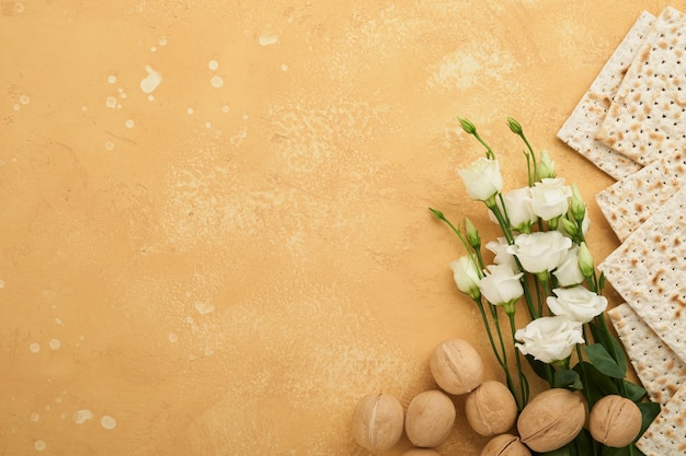 Pessach-Feier-Konzept Matzah koscherer Rotwein Walnuss und weiße und gelbe Rosen Traditionelles rituelles jüdisches Brot auf sandfarbenem altem Kachelwandhintergrund Pessach Jüdischer Feiertag Draufsicht