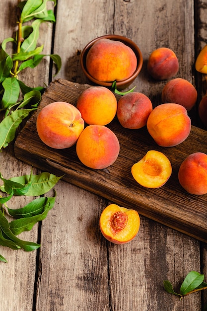 Pêssegos com folhas na placa de madeira escura com pêssego ao meio. Composição com pêssegos maduros e suculentos Colheita para alimentação. Frutas orgânicas frescas na velha mesa de madeira rústica.