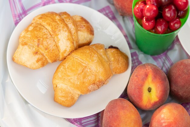 Pêssegos, croissants, frutas vermelhas em uma toalha de mesa em um piquenique