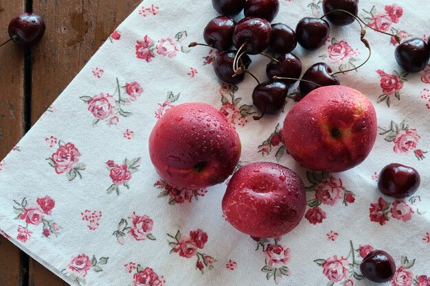 Pêssegos suculentos e cerejas cor de vinho repousam na toalha de mesa