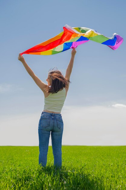 Pessoa acena uma bandeira LGBT arco-íris em pé com as costas