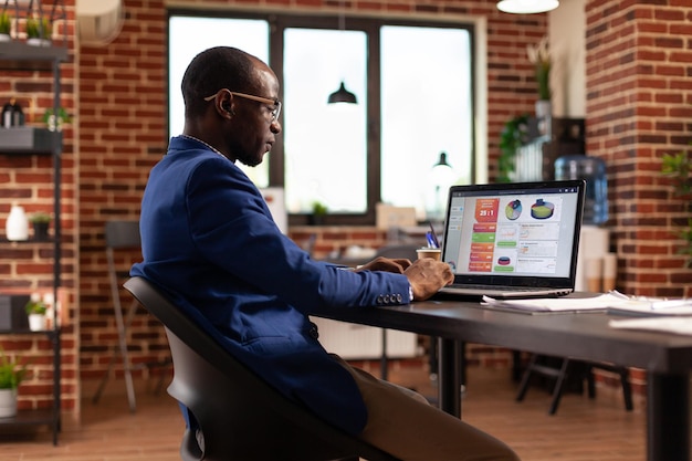 Pessoa afro-americana usando laptop para trabalhar em gráficos de negócios e crescimento financeiro. Homem de negócios trabalhando com computador para planejar o projeto e a estratégia de marketing para a empresa iniciante.