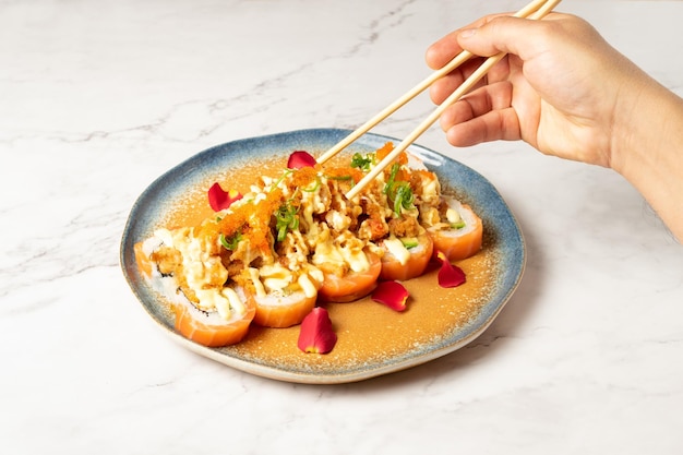 Pessoa anônima com pauzinhos de madeira comendo rolos de sushi variados com salada de caranguejo