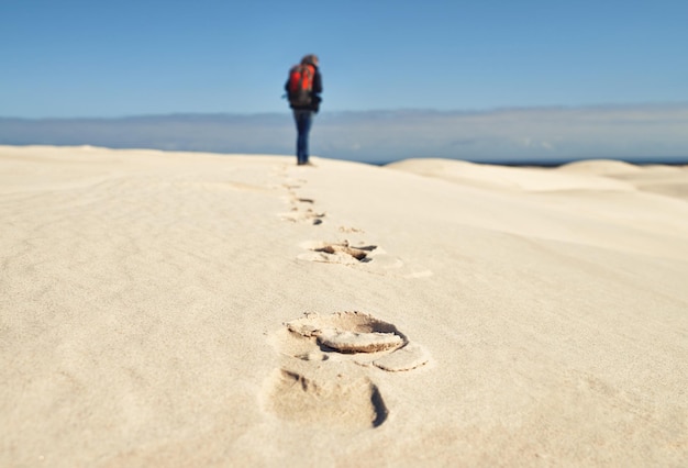 Foto pessoa caminhando e caminhando em dunas de areia para aventura de fitness no deserto e esportes extremos em clima árido atlético de volta ou equipamento de sobrevivência para exploração da natureza pegadas ou férias de paixão por caminhadas