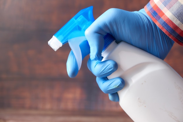 Pessoa com as mãos em luvas descartáveis usando spray desinfetante para limpar a superfície da mesa
