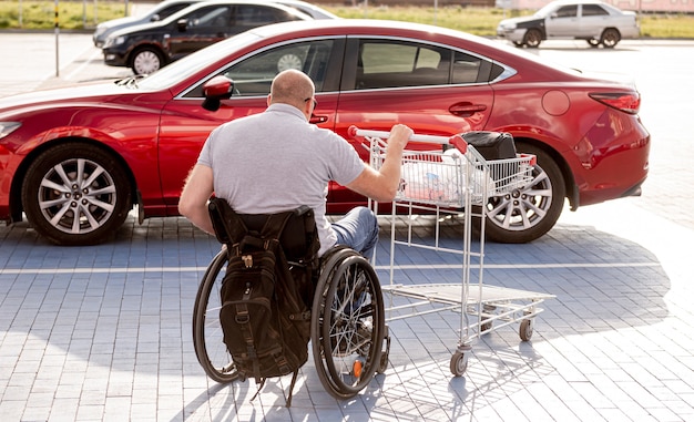 Pessoa com deficiência física empurra um carrinho em direção a um carro no estacionamento de um supermercado