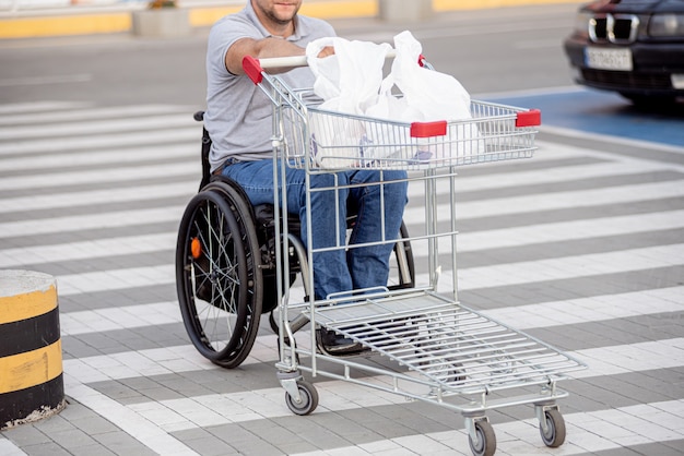 Foto pessoa com deficiência física empurrando carrinho na frente de si no estacionamento de um supermercado