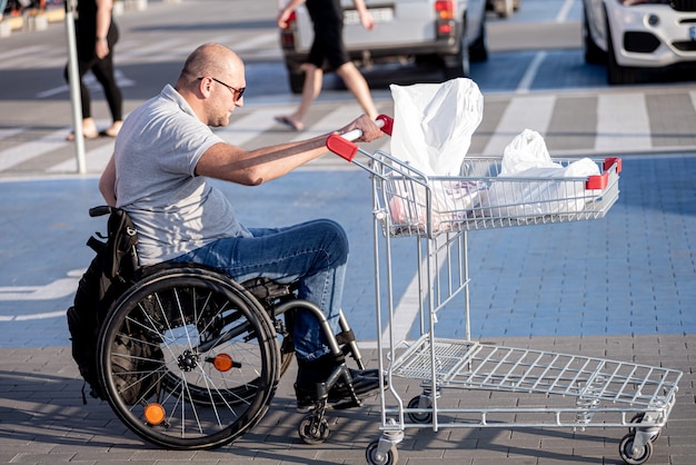 Foto pessoa com deficiência física empurrando carrinho na frente de si no estacionamento do supermercado