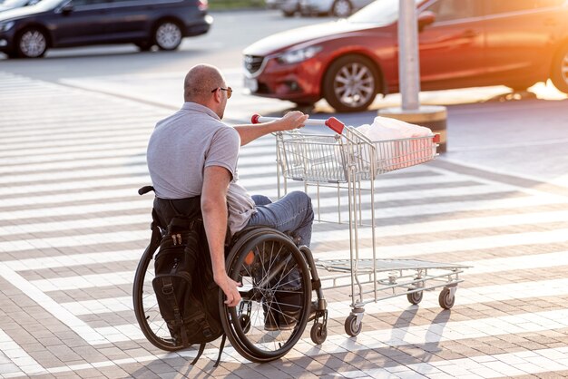 Pessoa com deficiência física empurrando carrinho na frente de si no estacionamento do supermercado