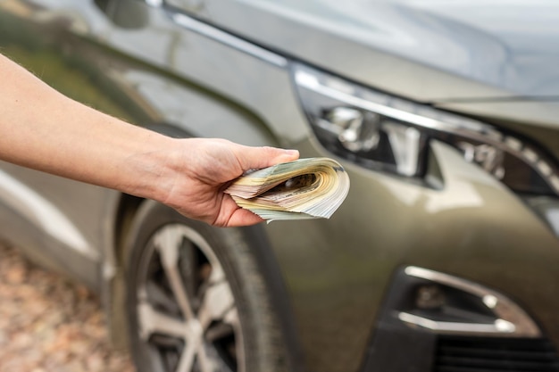 Pessoa com dinheiro na mão fica na frente do carro Empréstimo de seguro e compra do conceito de carro