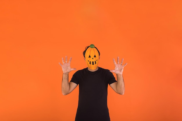 Pessoa com máscara de abóbora celebrando o Halloween assustando em fundo laranja Conceito de celebração Dia de Finados e Dia de Todos os Santos