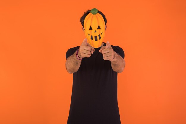 Foto pessoa com máscara de abóbora comemorando o halloween apontando para a câmera em fundo laranja conceito de celebração dia de todas as almas39 e dia de todos os santos39