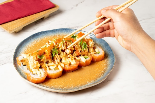 Pessoa com pauzinhos de madeira comendo rolos de sushi variados com salada de caranguejo servida