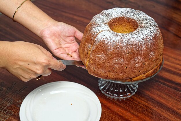 Pessoa cortando uma fatia de bolo de libra que está em uma base de vidro Close de um bolo de libra caseiro