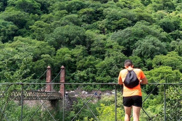 Pessoa da ravina Huentitan olhando para a vegetação da ravina trilhos de aço camiseta laranja mochila árvores e ponte guadalajara