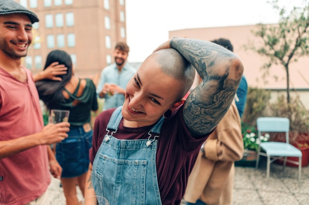 Pessoa de aparência androgênica com cabeça raspada e tatuagem sorrindo em festa