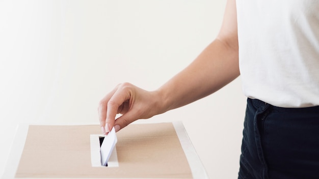 Foto pessoa de visão lateral que coloca uma cédula na caixa de eleição