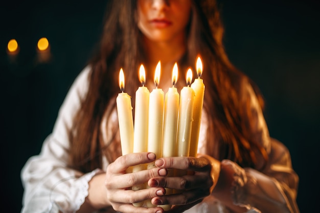 Pessoa do sexo feminino em camisa branca tem velas nas mãos. ritual de magia negra, ocultismo e exorcismo, adivinhação