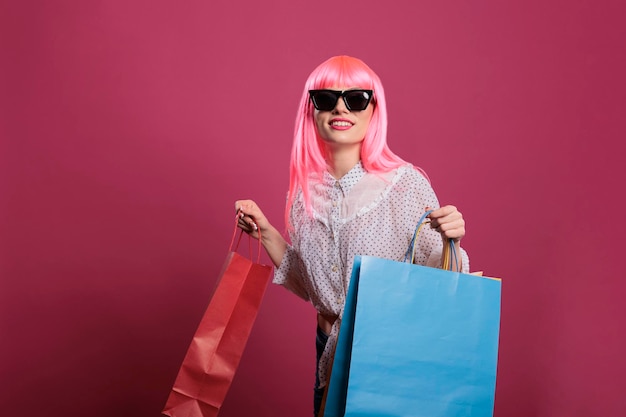 Pessoa elegante com óculos de sol carregando sacolas de compras depois de comprar roupas da loja de varejo no shopping, usando a compra com desconto de venda. Cliente elegante se sentindo feliz depois de pagar o dinheiro no pacote.