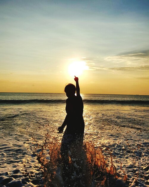Foto pessoa em silhueta de pé na praia contra o céu durante o pôr do sol