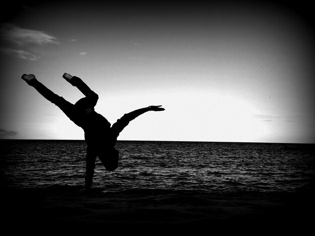 Foto pessoa em silhueta fazendo handstand na praia contra o céu