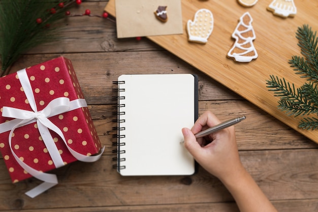 Foto pessoa, escrevendo no caderno aberto com caixa de presente e saborosos biscoitos caseiros de natal