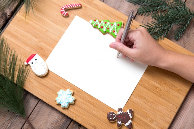 Foto pessoa, escrevendo no cartão de natal com biscoitos caseiros