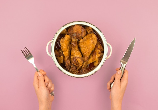 Pessoa faminta com um homem com garfo e faca pronto para comer frango assado em uma panela, conceito de fome infantil, foto da vista superior