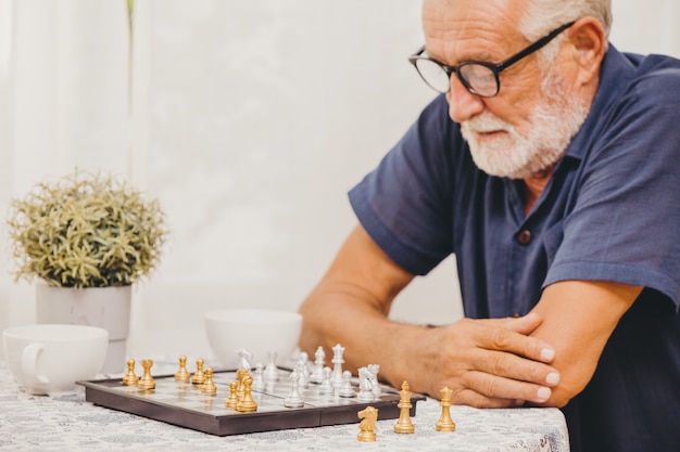 Pessoa idosa esperta que joga o jogo de mesa da xadrez em casa para treinar a memória cerebral e pensar o foco seletivo de sorriso feliz na parte de xadrez.