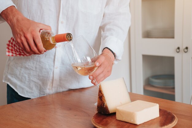 Pessoa irreconhecível agarrando uma taça de vinho branco com queijo ao lado para comer