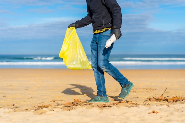 Pessoa irreconhecível da poluição do mar coletando plásticos na areia no conceito de ecologia da praia