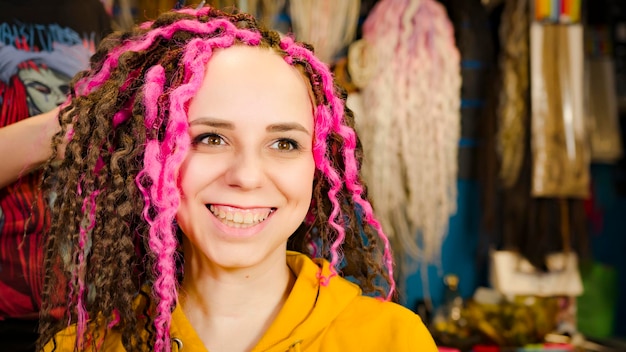 Pessoa irreconhecível faz penteado encaracolado para jovem no salão Cabeleireiro profissional faz dreadlocks rosa e marrom para cliente