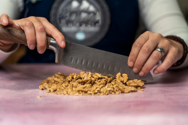 Pessoa irreconhecível usando uma faca para cortar nozes em pedaços pequenos para decorar alfajores argentinos caseiros. Conceito de comida regional e tradicional.