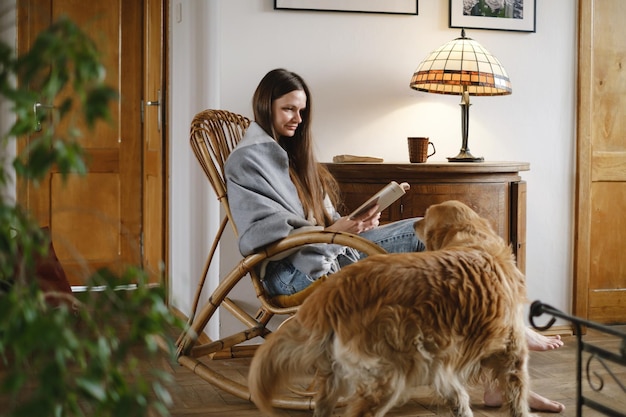 Pessoa lendo com cachorro golden retriever na cadeira de balanço em casa