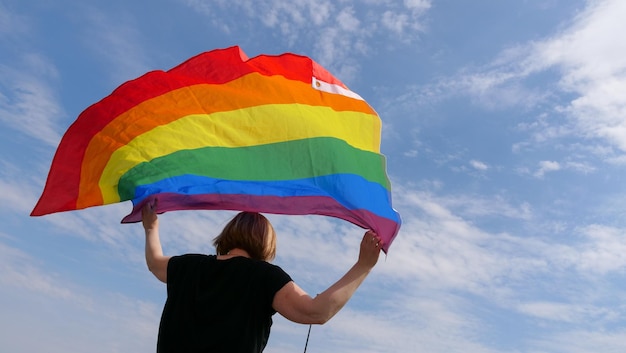 Pessoa LGBT segurando a bandeira LGBT no fundo do céu