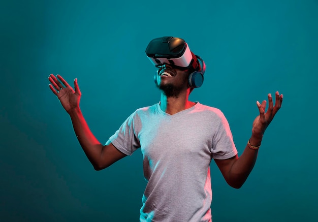 Pessoa milenar usando óculos vr para jogar online, tentando simulação futurista 3d sobre fundo azul. Jovem adulto brincando com tecnologia de realidade virtual no fone de ouvido interativo para se divertir.