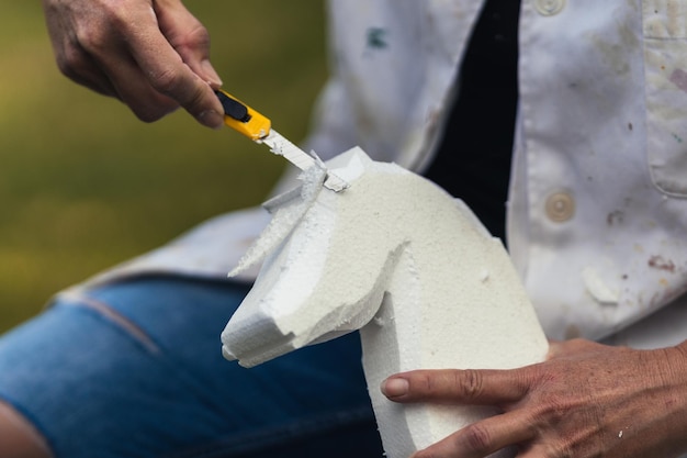 Pessoa moldando um pedaço de poliestireno para criar a figura de um animal