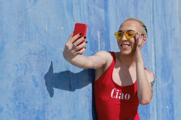 Pessoa não binária sorridente, tirando uma selfie com um telefone celular ao ar livre na rua. conceito de gênero não binário.