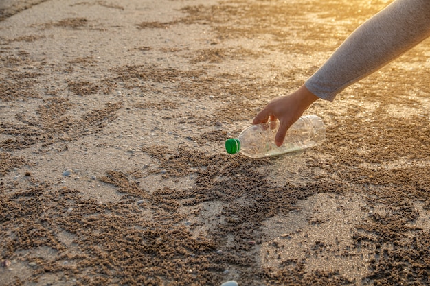 Pessoa pegando garrafa de plástico de limpeza na praia