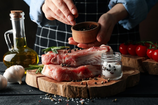 Pessoa polvilha especiarias na carne crua. Cozinhar o conceito de bife