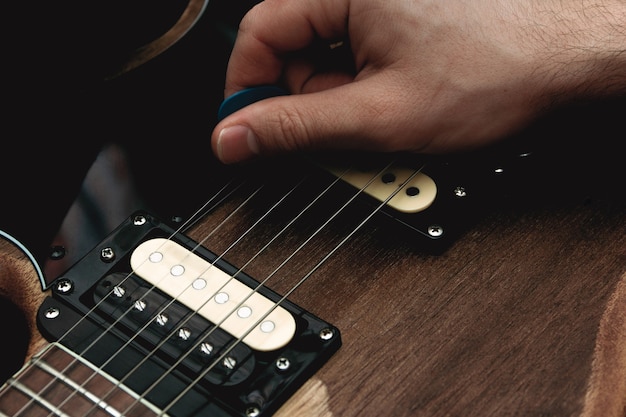 Pessoa que dedilha as cordas de uma guitarra elétrica com uma palheta. Foco seletivo. Copie o espaço.